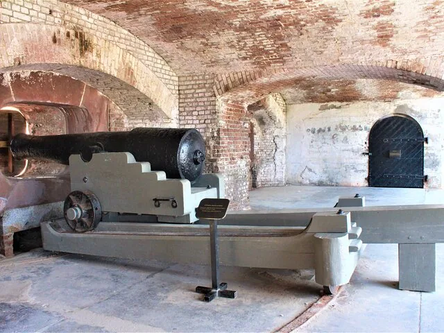 A large black cannon on a wooden carriage inside a brick fort structure.