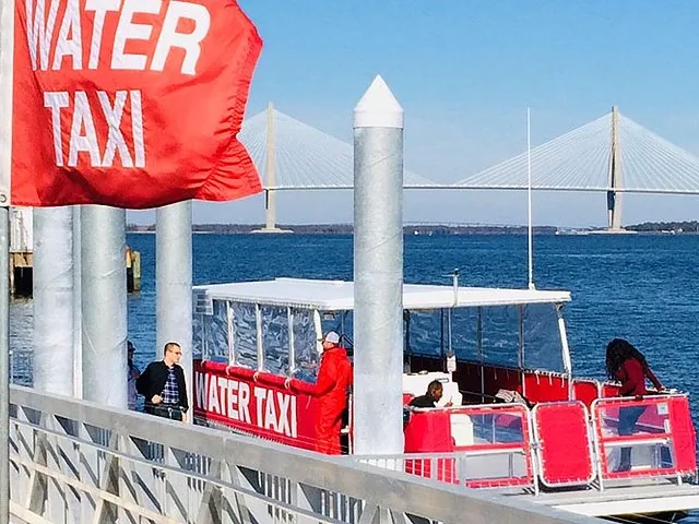 A red and white water taxi docked at a pier, with a bridge in the distance.