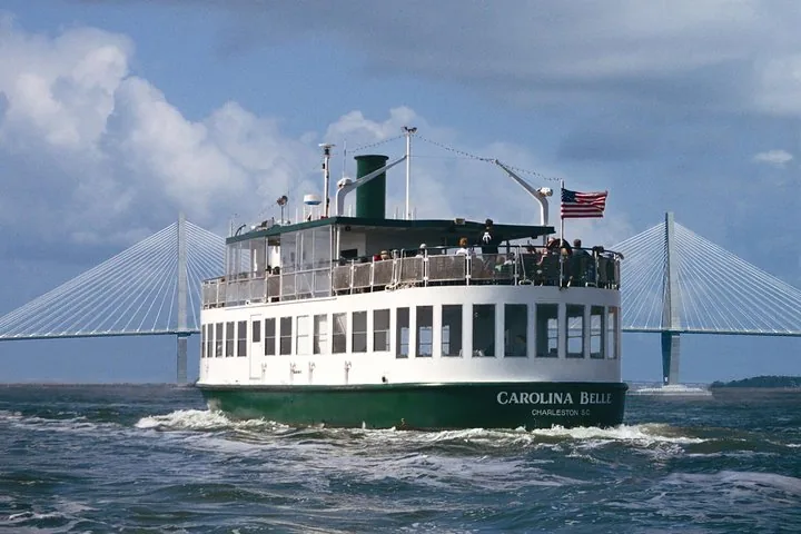 Ein Passagierschiff fährt auf dem Wasser mit einer Brücke im Hintergrund.