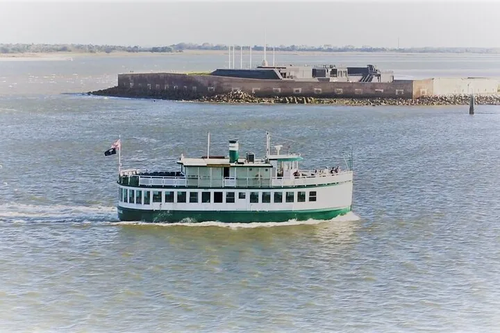 Ein grün-weißes Passagierschiff fährt in der Nähe eines historischen Forts auf einer Insel.