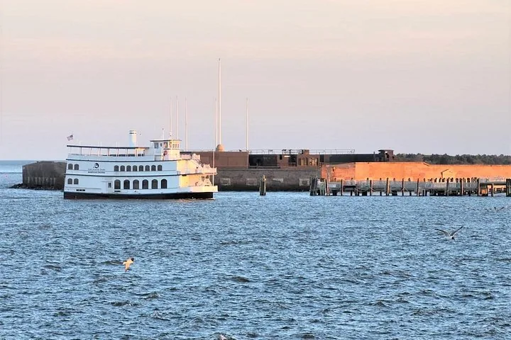 Un bateau de passagers blanc navigue devant un fort historique sur l'eau.
