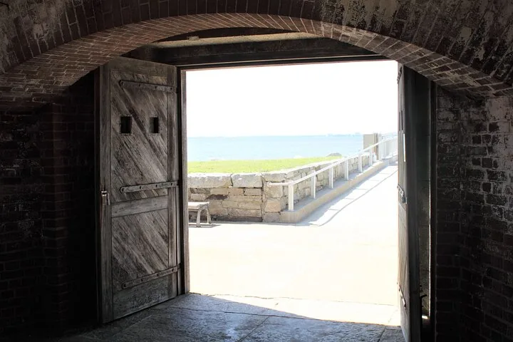 Vue à travers les portes en bois ouvertes d'un fort en briques donnant sur l'eau.